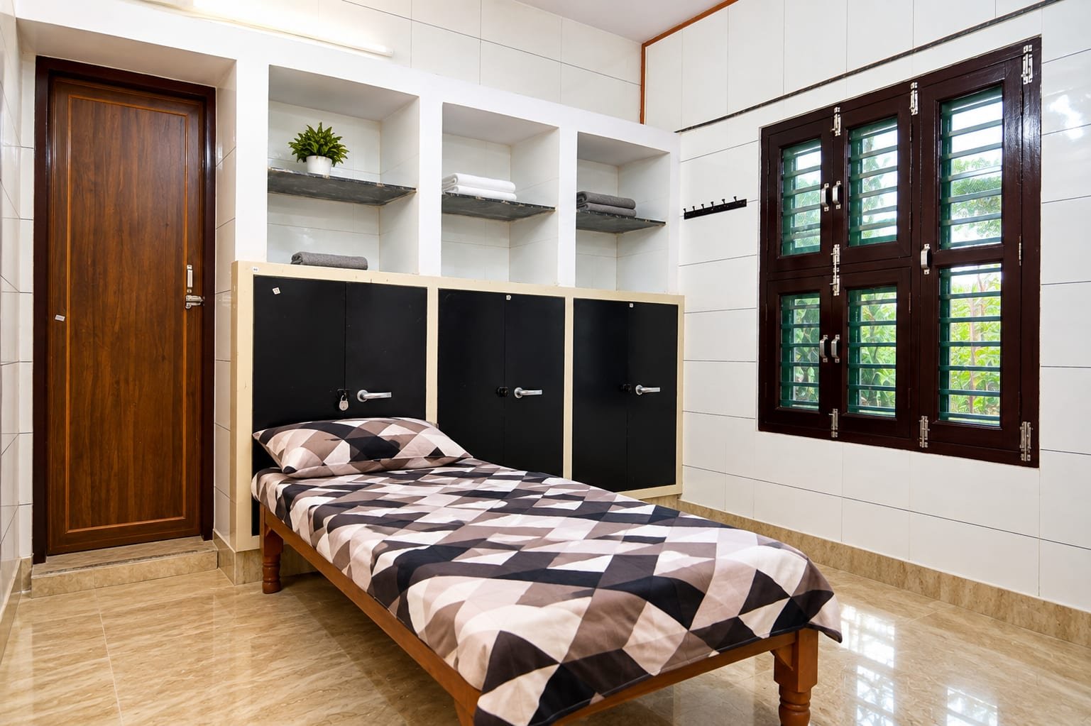 A single room with one bed, three lockers with open shelves above them and a window looking onto trees
