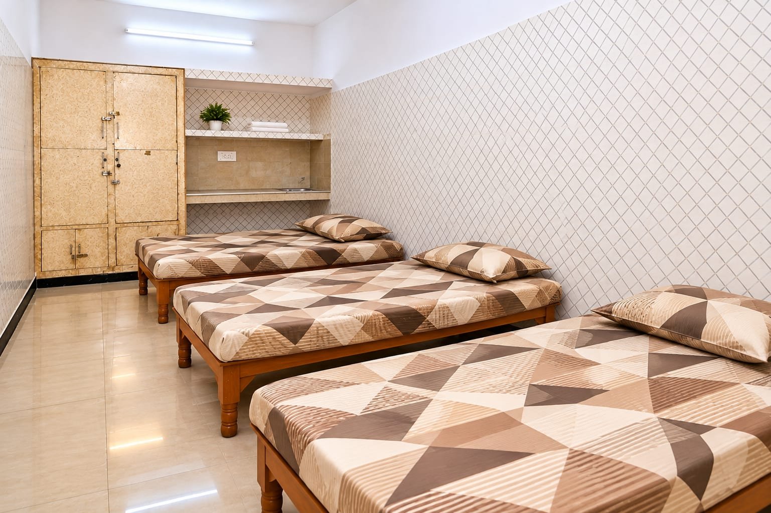 A triple-sharing room with three beds, a wooden almirah and a study counter along the wall